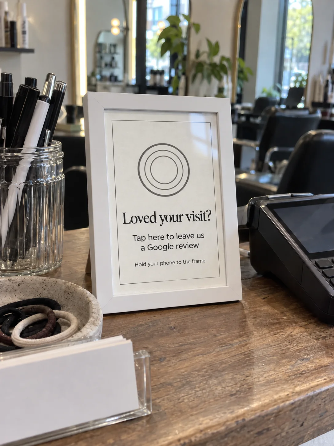 The White TapIt Frame on its stand on a café counter beside a card reader and a tip jar